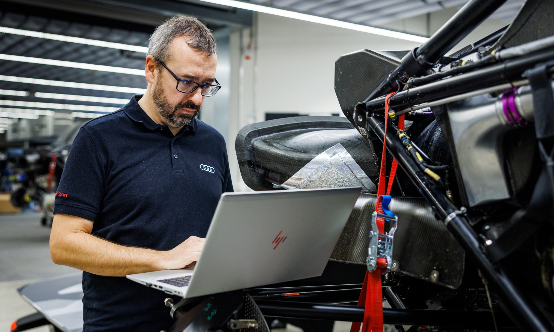 Arnau Nibuó Bosch i en arbeidssituasjon ved datamaskinen ved siden av den demonterte Audi RS Q e-tron.